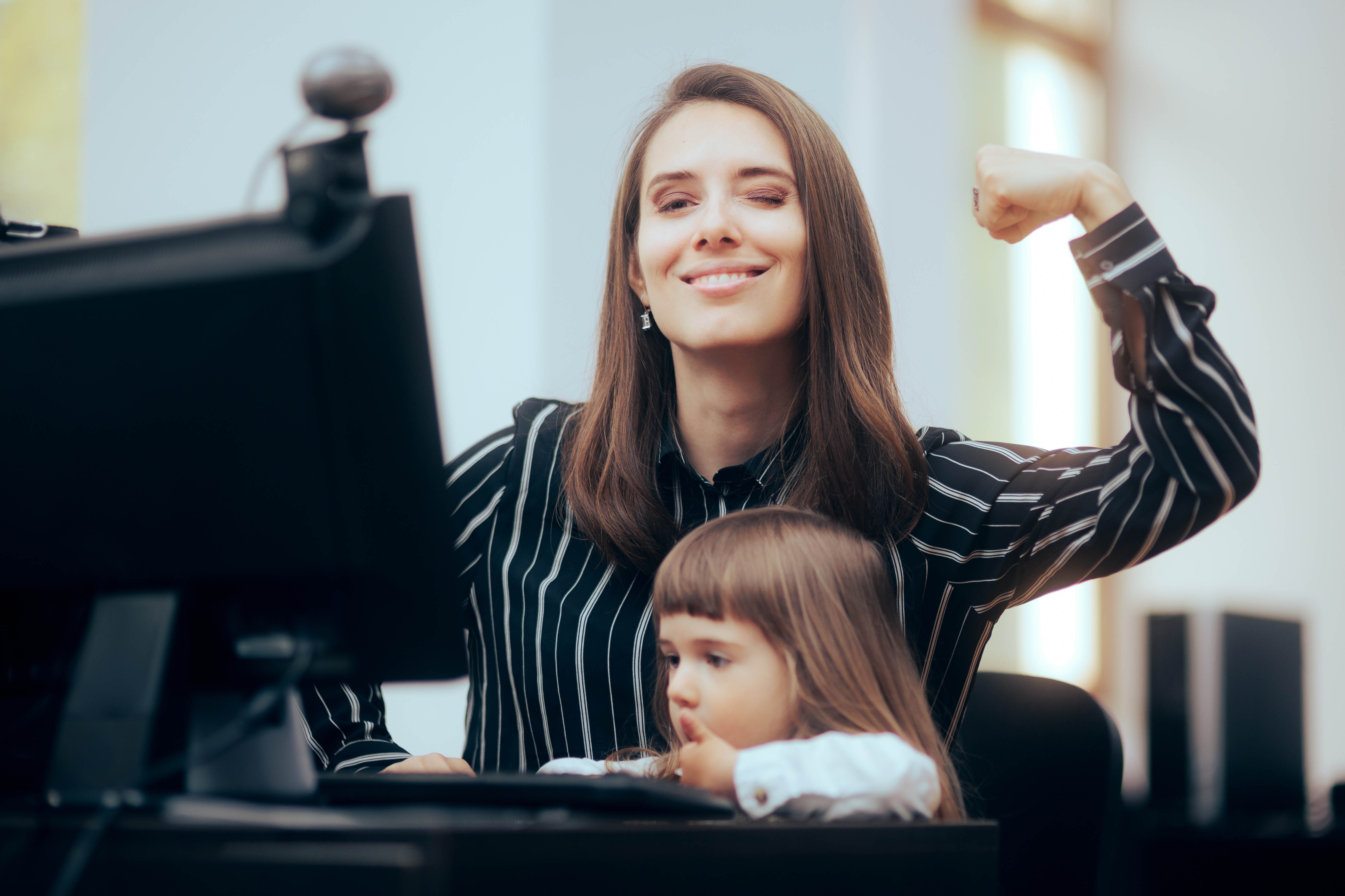 Professional looking young woman poses looking at the camera with her arm flexed, while a female toddler sits on her lap playing with the computer Professional looking young woman poses looking at the camera with her arm flexed, while a female toddler sits on her lap playing with the computer
